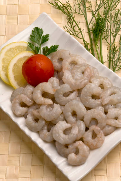 istock uncooked raw headless Shrimps with lemon slice and tomato on white plate with Bamboo matt 687690198