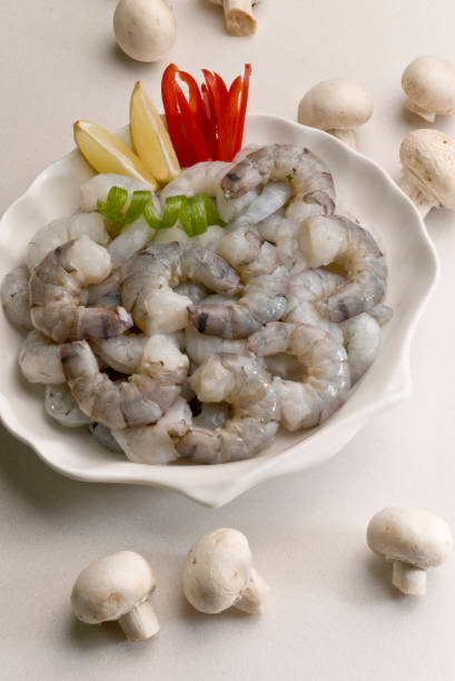 istock uncooked raw headless Shrimps with lemon slice and tomato on white plate with white background 687690234