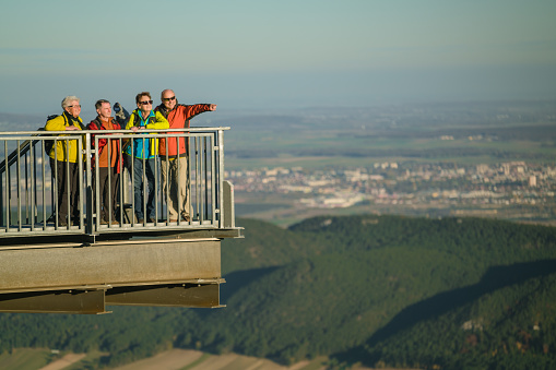 four seniors in colorful hiking outfit overlooking the beautiful rural landscape from a very high viewpoint