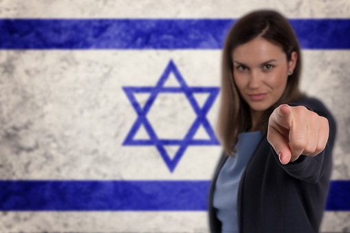 Beautiful businesswoman pointing her finger at you Israel flag background.