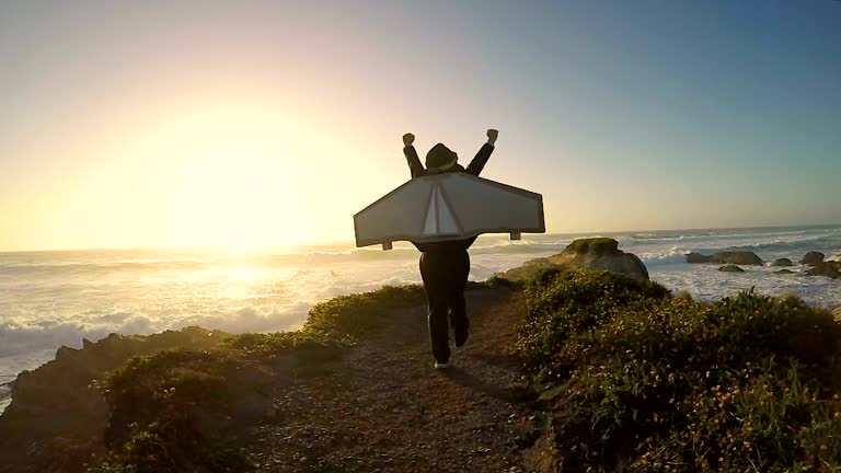 A young boy dressed in business suit and jet pack imagines flying his business to the next level and bringing in record earnings. He runs away from the camera along the coastline and beach in San Luis Obispo County, California.