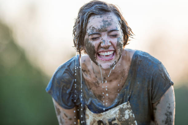 Smiling Victory Beautiful young woman covered in mud and dirt laughing and smiling leaning forward as a teammate dumps water on her head in celebration after a long race. individual sports stock pictures, royalty-free photos & images