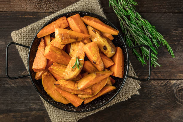 Overhead photo of roasted sweet potatoes in pan An overhead photo of roasted sweet potatoes in a pan, shot from above on dark rustic wooden textures with rosemary branches, with a place for text sweet potato french fries stock pictures, royalty-free photos & images
