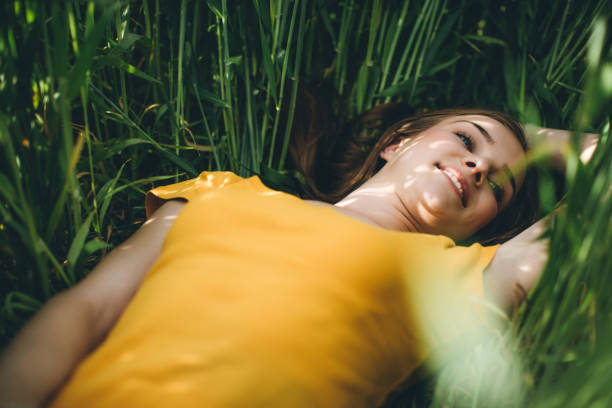 Teenage girl with red hair lying on green grass with eyes closed. Outdoor portrait photography. Relaxation and nature concept.