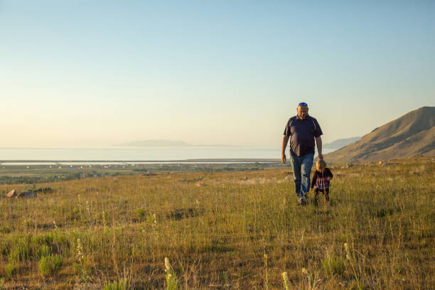 Young toddler girl with blonde hair walking in field with her father in late afternoon Young toddler girl with blonde hair walking in field with her father in late afternoon. Subjects are backlit. Tooele, Utah along benches of Oquirrh Mountains. tooele stock pictures, royalty-free photos & images