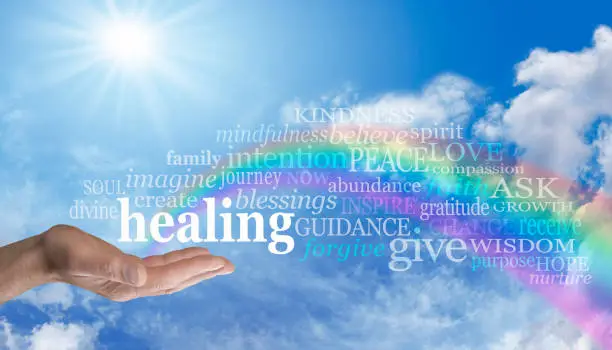 Blue sky and clouds with a man's hand palm up and the word 'healing' surrounded by a relevant word cloud and a rainbow arcing out of his palm with the words floating across the rainbow