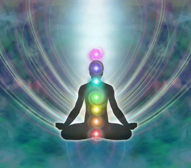 Silhouette of a man in lotus meditation position with Seven Chakras on blue background with kundalini energy flowing downwards