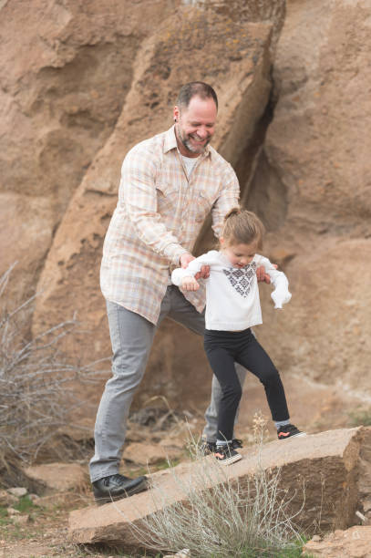 istock Modern looking dad helps his young daughter climb over rocks while they explore a nature area on a hike 687790948