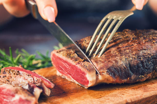 Cutting Juicy Beef Steak Young women cutting medium roasted beef steak on the wooden board rare stock pictures, royalty-free photos & images