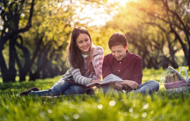 istock Children reading a book together sitting in the park 687810468