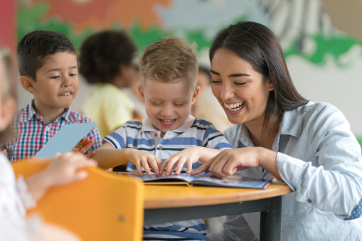 Portrait of a happy Latin American teacher reading a book with a student at the school and having fun - education concepts