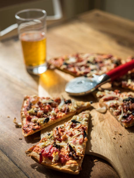 Home made oven baked Pizza with variety of topings on the wooden table with pizza cutter. Glass of Lager beer in the background.