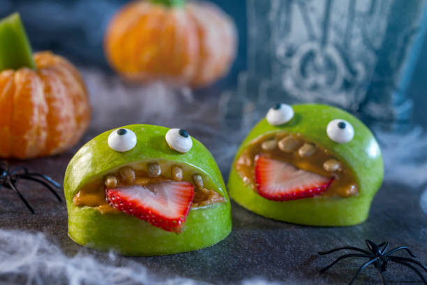 Healthy Halloween Apple Monsters Fruit Kids Treat Healthy Halloween candy alternative fruit. Apple monsters made of peanut butter, sunflower seeds and candy eye balls with spiders, spider webs, and tangerine pumpkins with celery stem on haunted halloween night. halloween food stock pictures, royalty-free photos & images