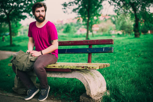 istock Bearded hipster with a backpack sitting on the bench on a sunny day 687853220