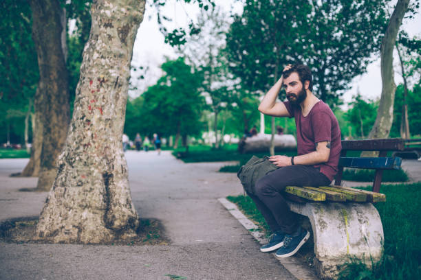 Bearded hipster with a backpack sitting on the bench on a sunny day