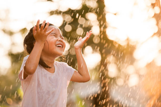 feliz niña asiática divertirse para jugar con la lluvia - innocence fotografías e imágenes de stock