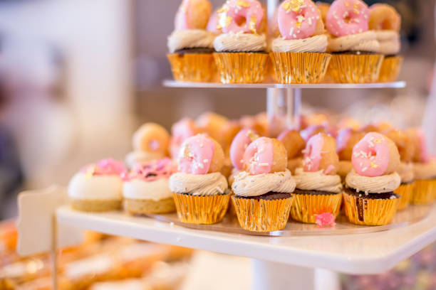 디저트 테이블에 미니 핑크 도넛을 얹은 미니 초콜릿 컵 케이크. 그들은 계층된 디스플레이 트레이에 표시 됩니다. - icing cake multi colored weddings 뉴스 사진 이미지