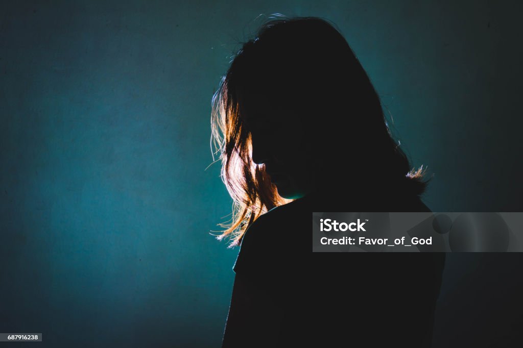 silhouette of depress woman standing in the dark with light shine behind Women Stock Photo