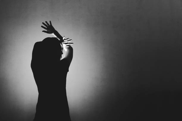 istock woman afraid of something, covering face and head with light behind 687916454