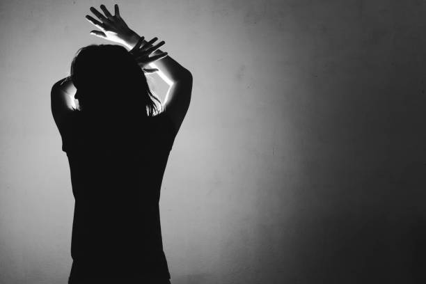 istock woman afraid of something, covering face and head with light behind 687916484