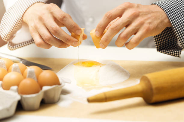 massa de pastel - chef quebrando ovo em heap de farinha - cake making mixing eggs - fotografias e filmes do acervo