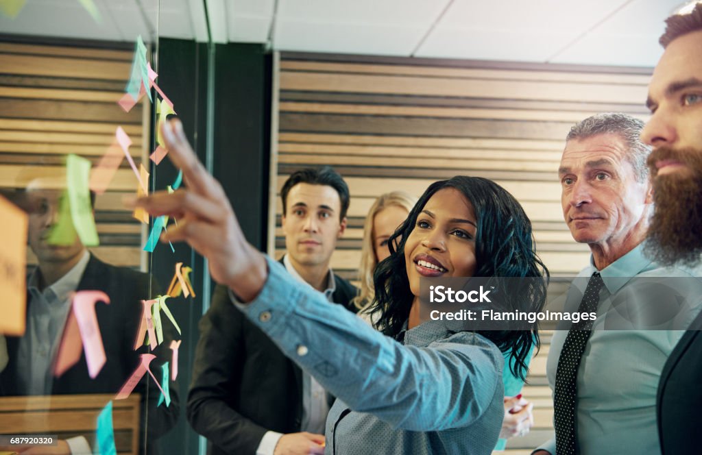 Woman explaining the plan to office team Young smiling black businesswoman at the wall with stickers communicating with her colleagues. Mixed team of entrepreneurs Leadership Stock Photo