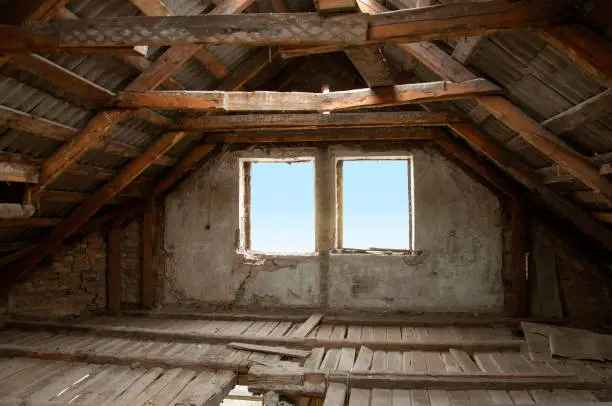 The process of building reconstruction. An old attic loft with a wooden roof, broken floors and brick walls.