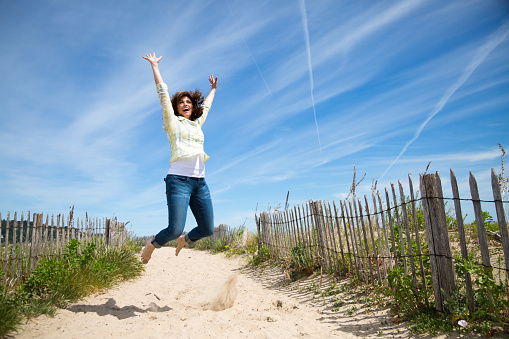 Happy middle aged woman jumping on the beach crazy for vacation