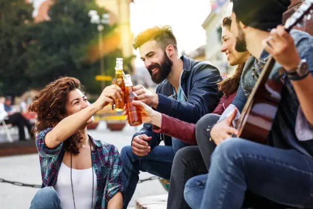 Group of young friends hangout on street in downtown.They standing by the city square,drinking and toasting with beer.