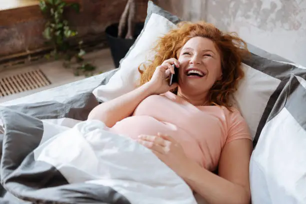 Laughing out loud. Expectant mother laughing and crying in turn during a telephone conversation with friend.