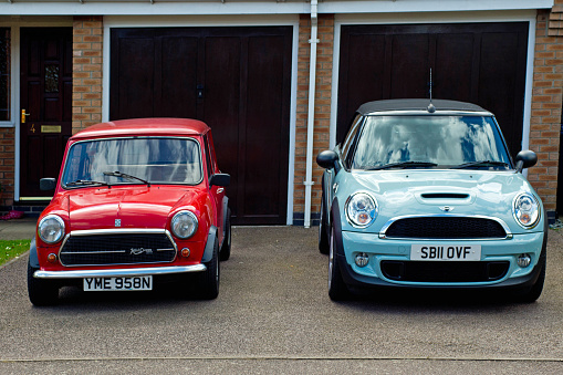 Huntingdon, UK, July, 03, 2016. An exterior view of a classic Innocenti Mini Cooper 1300 Export in red and a new BMW MIni Cooper S convertible in blue on the drive of their owner. The shot is taken from the front of the drive and shows both cars front on.The Innocenti was produced under licence in Italy and then exported around the world.