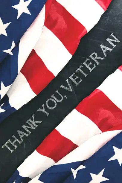 Top view of two fabric flags of America with text of thank you, veterans written on the chalkboard