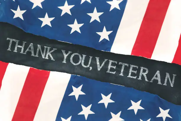 Two American flags made out of paper with text of thank you, veteran on the chalkboard