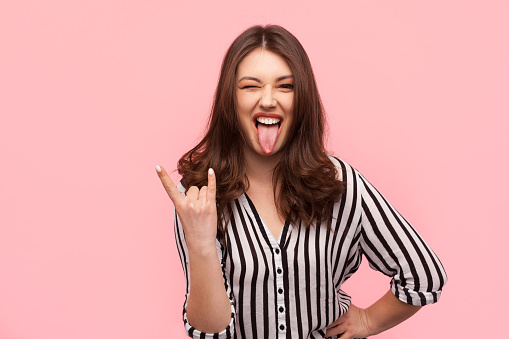 Young trendy girl showing tongue out and gesturing rock sign.