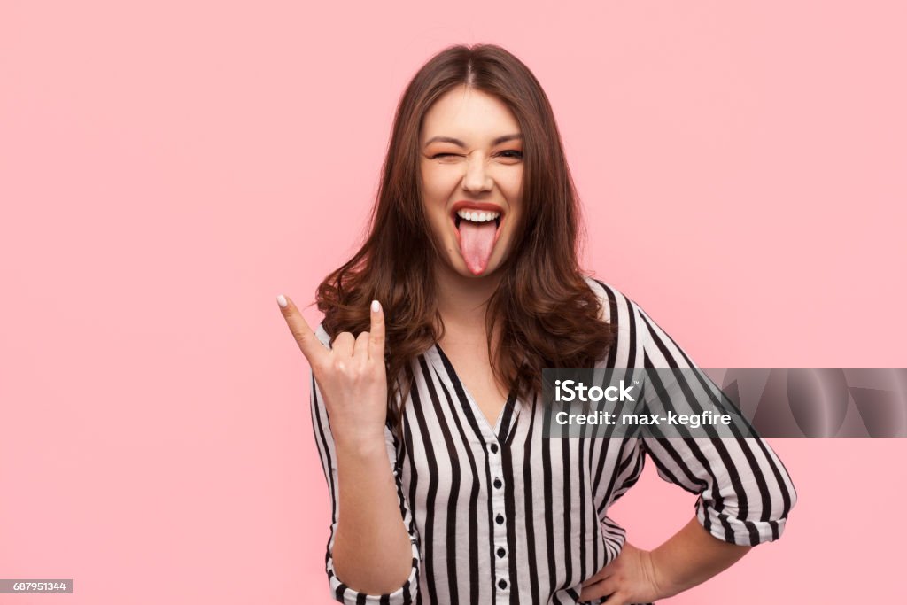 Stylish girl gesturing on pink background Young trendy girl showing tongue out and gesturing rock sign. Women Stock Photo