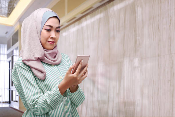 hermosa mujer asiática con hijab sosteniendo teléfono inteligente - indonesia fotografías e imágenes de stock