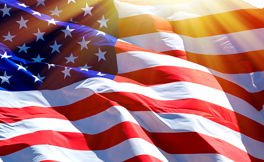 A large USA flag of stars and stripes flying high in strong wind on a sunny day in springtime.