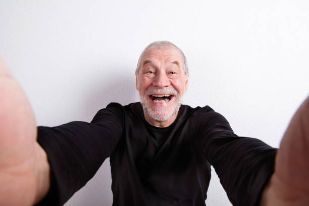 Senior man in black t-shirt, taking selfie, studio shot.