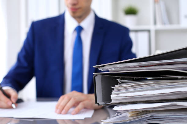 binders with papers are waiting to be processed with businessman back in blur. accounting planning budget, audit, insurance  and business concept - tax tax form law business imagens e fotografias de stock