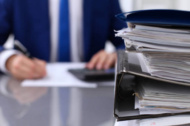 istock Binders with papers are waiting to be processed with businessman back in blur. Accounting planning budget, audit, insurance  and business concept 688001700