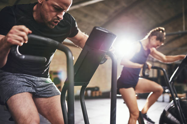 istock Man and woman riding cycling machines grimacing 688008480