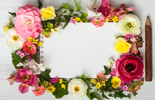 Blank notepad,pen and flowers over white wooden background. Top view with copy space