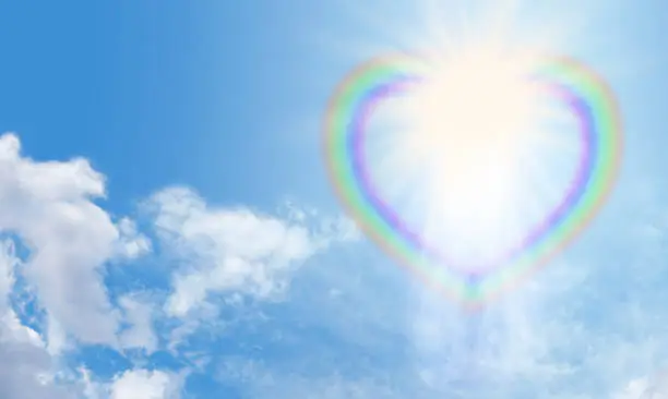 Transparent heart shaped rainbow bursting with white light on a blue sky background