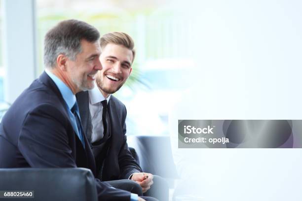 Mature Businessman Using Digital Tablet To Discuss Information With A Younger Colleague In A Modern Business Lounge Stock Photo - Download Image Now