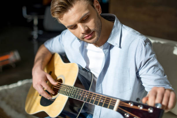 istock Young handsome pensive man playing guitar on sofa 688033798