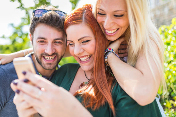 Group of friends with smartphone having fun together at park. Best friends, two girls and a boy smiling and looking at the phone. Lifestyle and friendship concepts