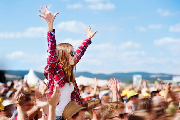 Teenagers at summer music festival enjoying themselves Teenage couple at summer music festival under the stage in a crowd enjoying themselves. Handsome man giving beautiful young woman piggyback, arms in the air. concert stock pictures, royalty-free photos & images