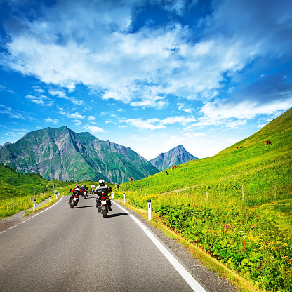 Group of motorcyclists on countryside in mountains, traveling along Alpine mountains, extreme sport, driving along cow pasture