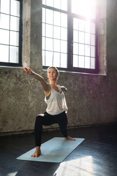 Young woman practicing yoga in an urban loft: Warrior 2 pose Young woman practicing yoga in an urban loft warrior 2 stock pictures, royalty-free photos & images