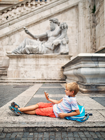 Kids visiting Rome, Italy. Little boy is resting in Piazza del Campidoglio, in front of Fontana della Dea Roma. The boy aged 7 is mimicking the statue of River Nile in the background.
